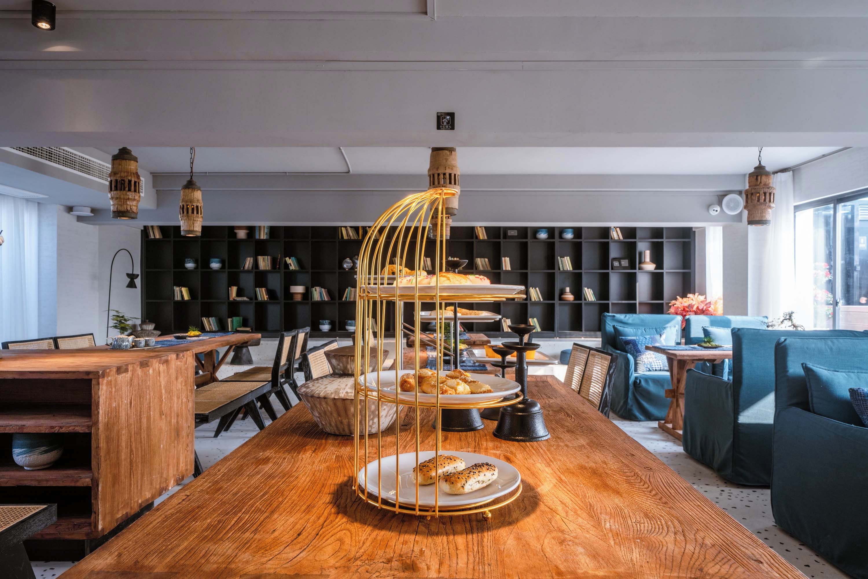 A modern interior with a wooden dining table, a three-tiered dessert stand, and a bookshelf in the background.