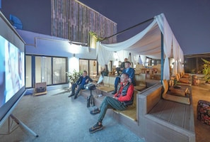 An outdoor seating area with a modern design, including a large screen for presentations and comfortable seating arrangements.