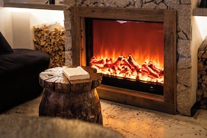 A fireplace with a stone surround, a log pile, and a book on a wooden stump.