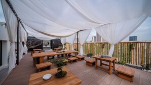 Een terras buiten met houten tafels en banken, een barbecue en een bamboombordering.