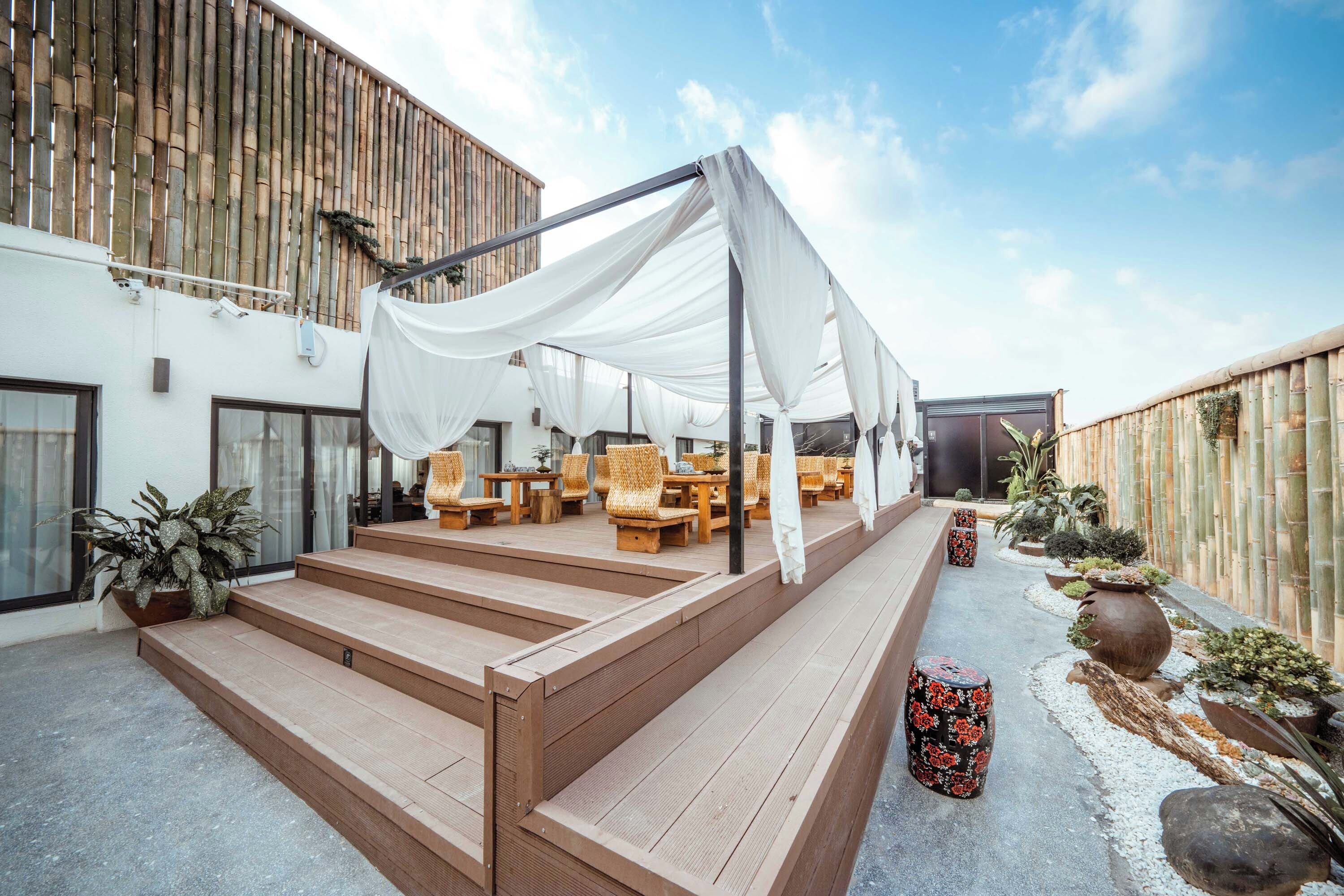 A covered outdoor seating area with wicker furniture, a wooden staircase, and a bamboo fence.