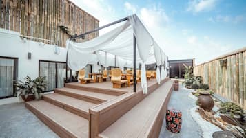 A covered outdoor seating area with wicker furniture, a wooden staircase, and a bamboo fence.