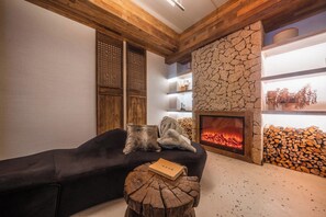 A cozy living room with a fireplace, wooden beams, and a stone wall.