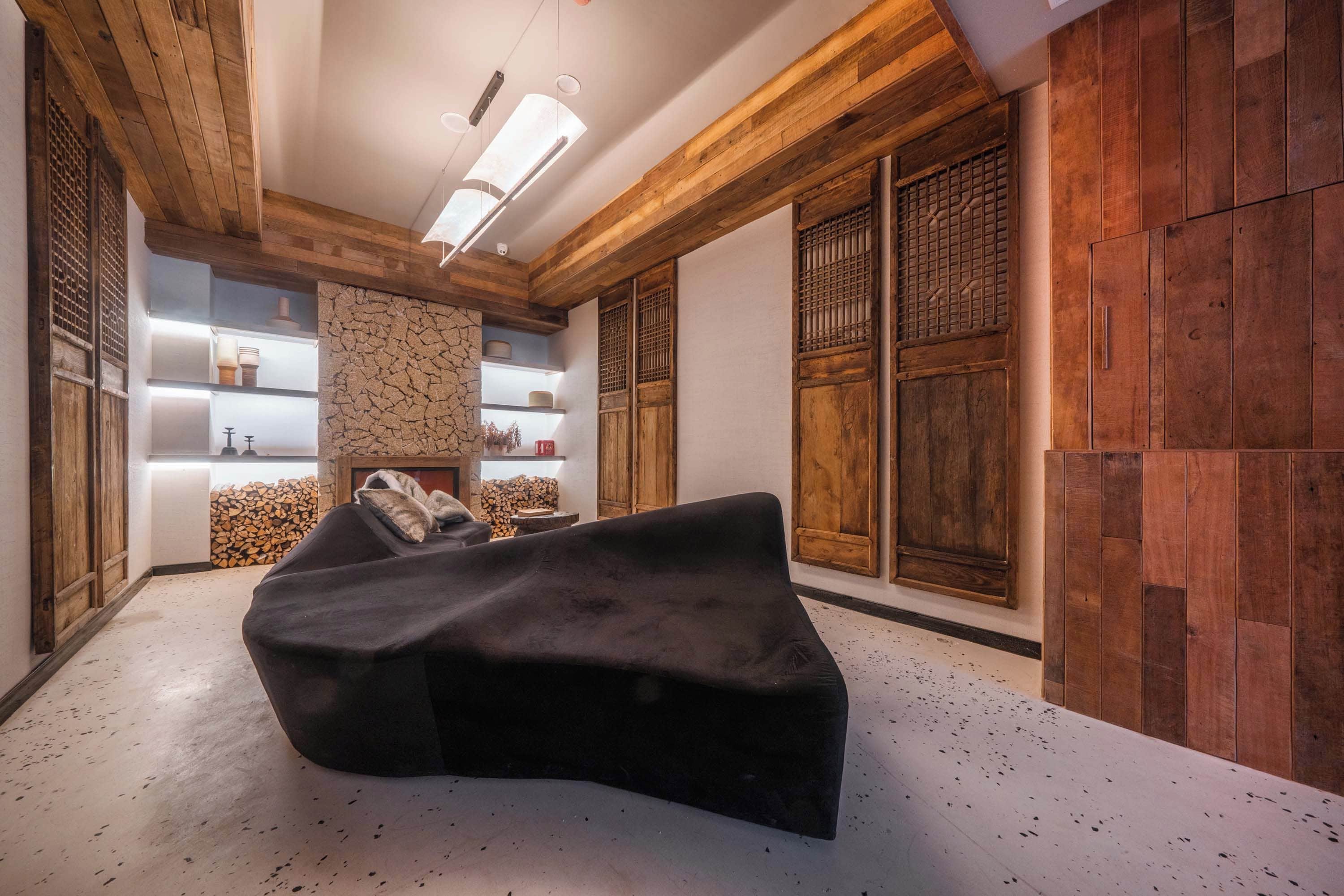 Sala de estar moderna com sofá preto curvado, vigas de madeira e parede de pedra.