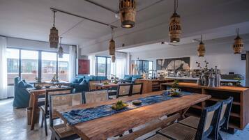 A spacious dining area with wooden tables and chairs, hanging wooden light fixtures, and large windows offering views of the cityscape.