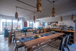 A spacious dining area with wooden tables and chairs, hanging wooden light fixtures, and large windows offering views of the cityscape.