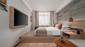 Habitación de hotel moderna con una cama grande, televisor en la pared, escritorio con lámpara y vistas al exterior a través de la ventana.