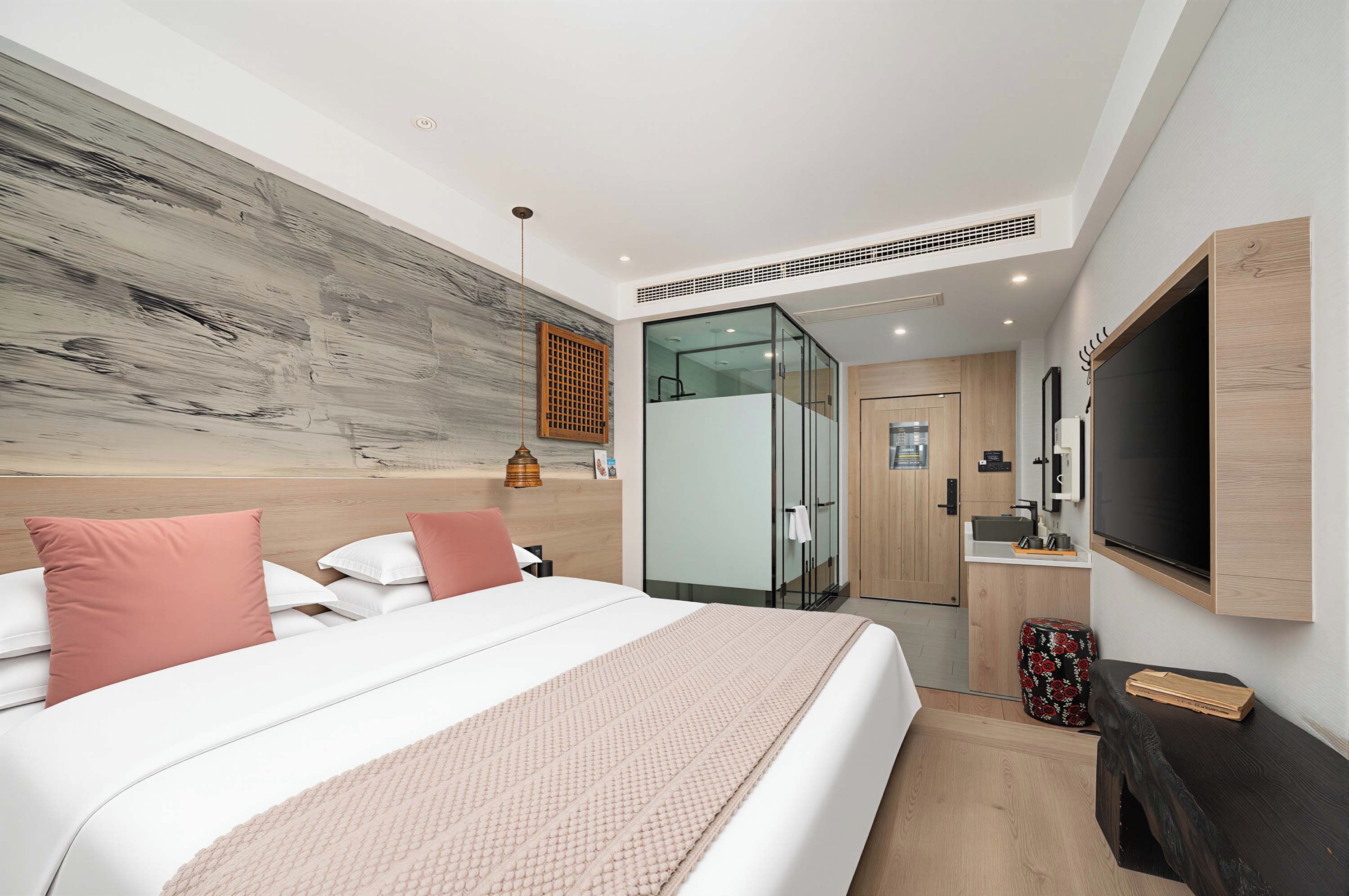Habitación de hotel moderna con una cama grande, un televisor de pantalla plana, un panel de madera decorativo y una cabina de ducha de vidrio.