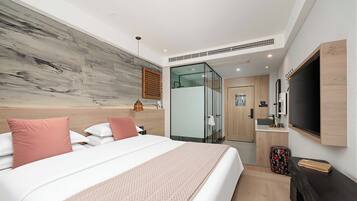 Habitación de hotel moderna con una cama grande, un televisor de pantalla plana, un panel de madera decorativo y una cabina de ducha de vidrio.
