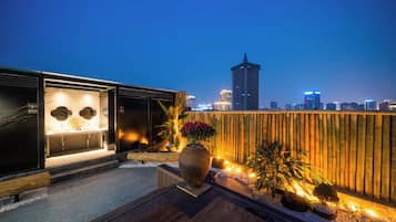 Una terraza en la azotea de diseño moderno, con zona de estar, una maceta grande con flores y vistas al horizonte de la ciudad al anochecer.