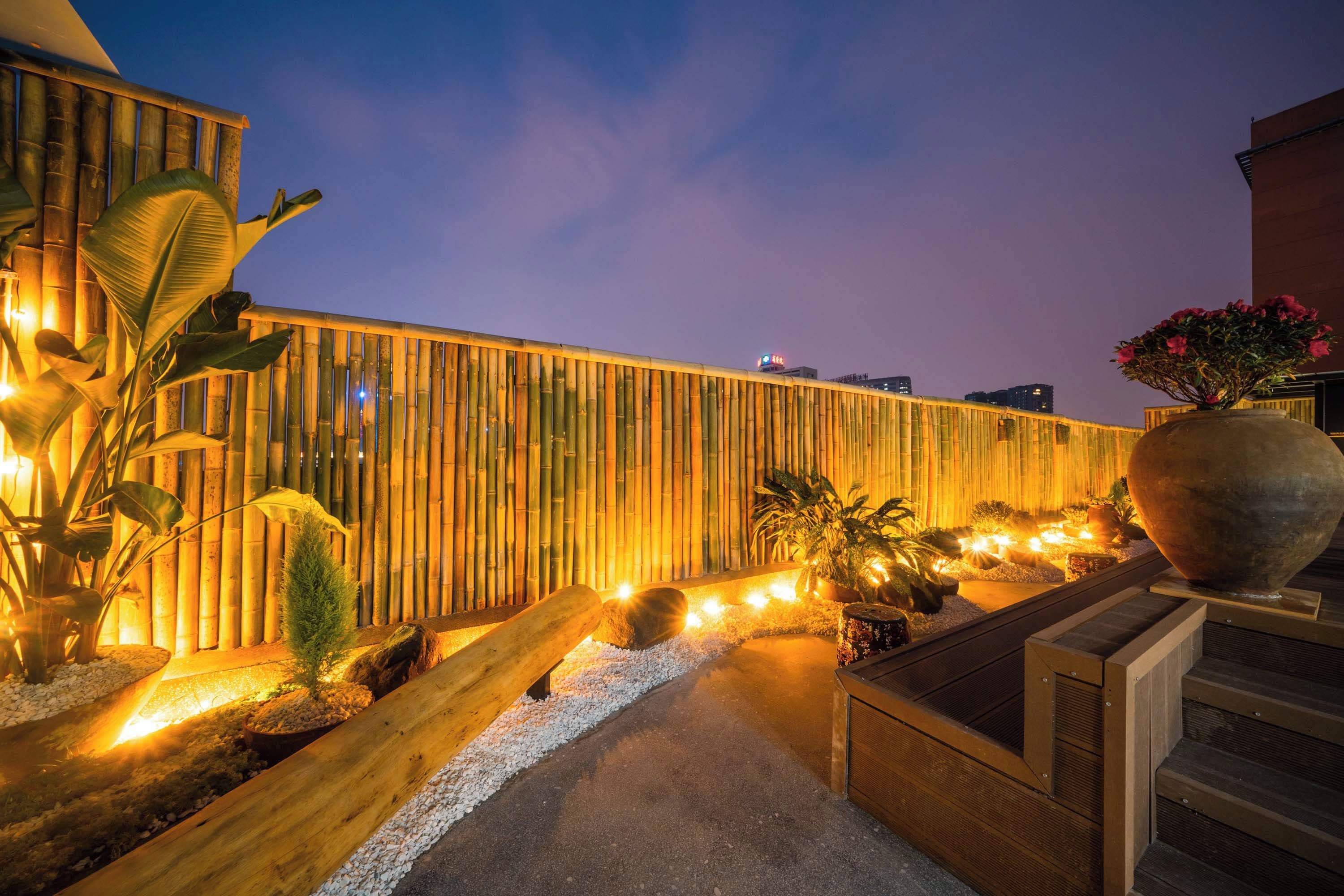 Una cerca de bambú, plantas en macetas y un sendero que conduce a la entrada de un edificio.