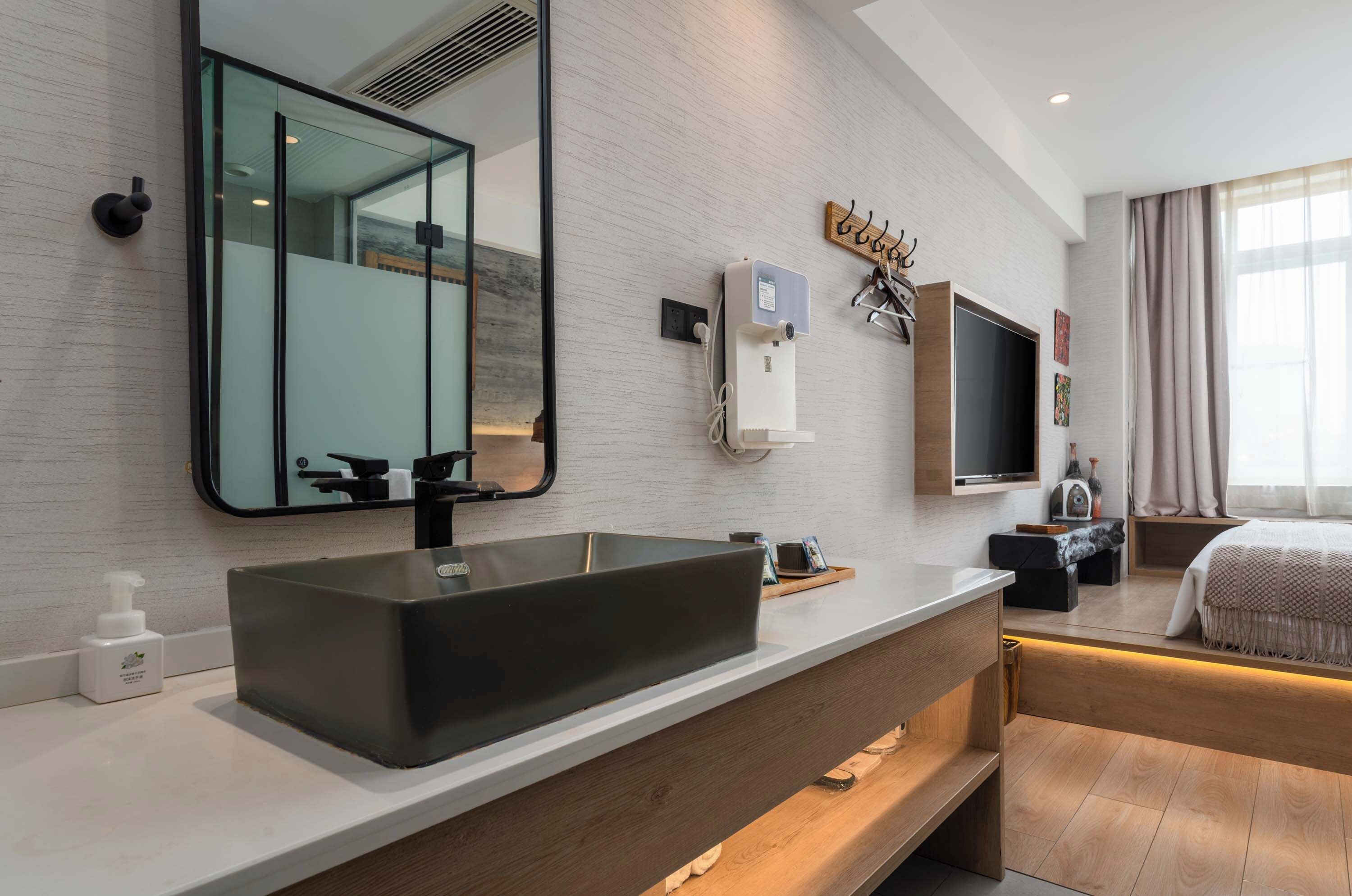 Un baño moderno con un espejo grande, un lavamanos negro y un mueble de tocador con gabinete de madera.