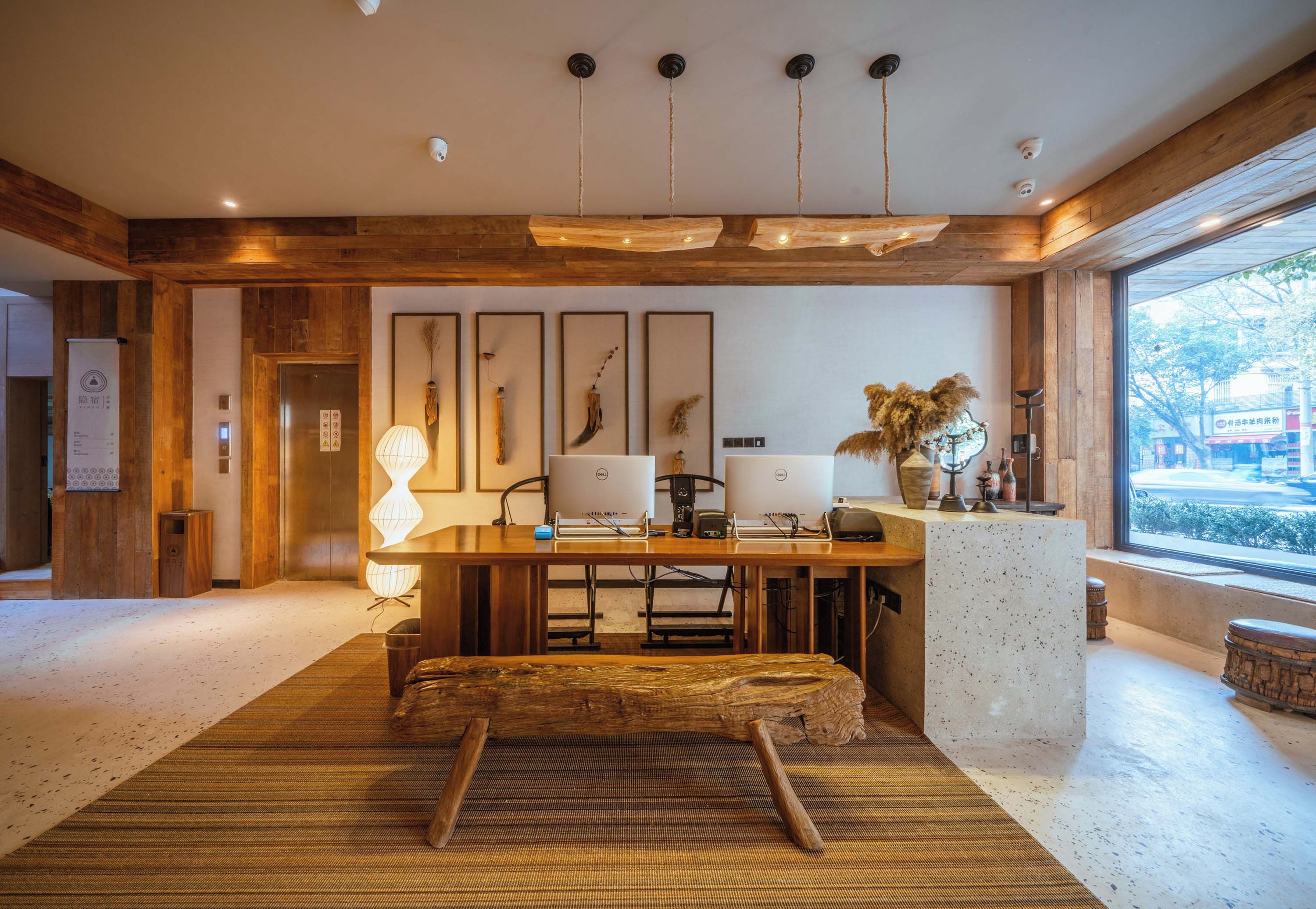 A modern interior with a wooden ceiling, a central desk with two computers, a large window, and a view of the outside.
