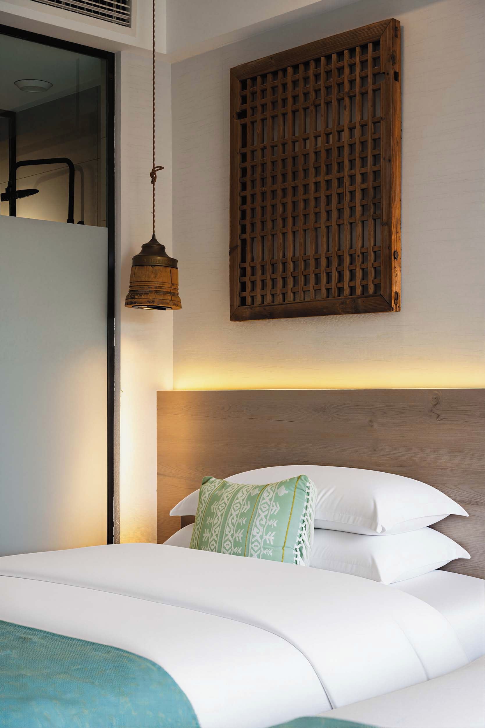 A hotel room with a bed, a hanging light fixture, and a wooden headboard.