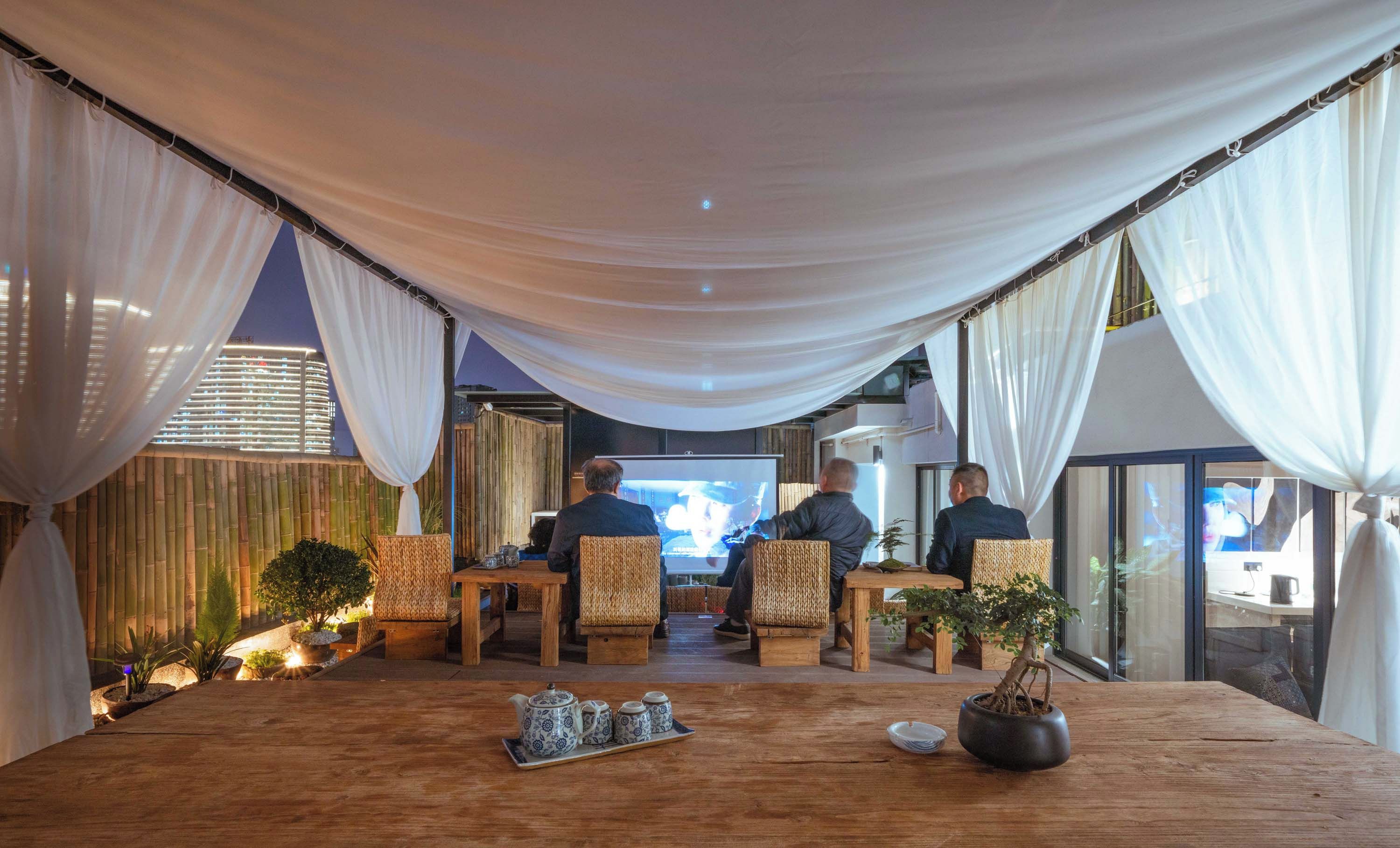A room with a large table, chairs, a television screen, and a view of a cityscape.