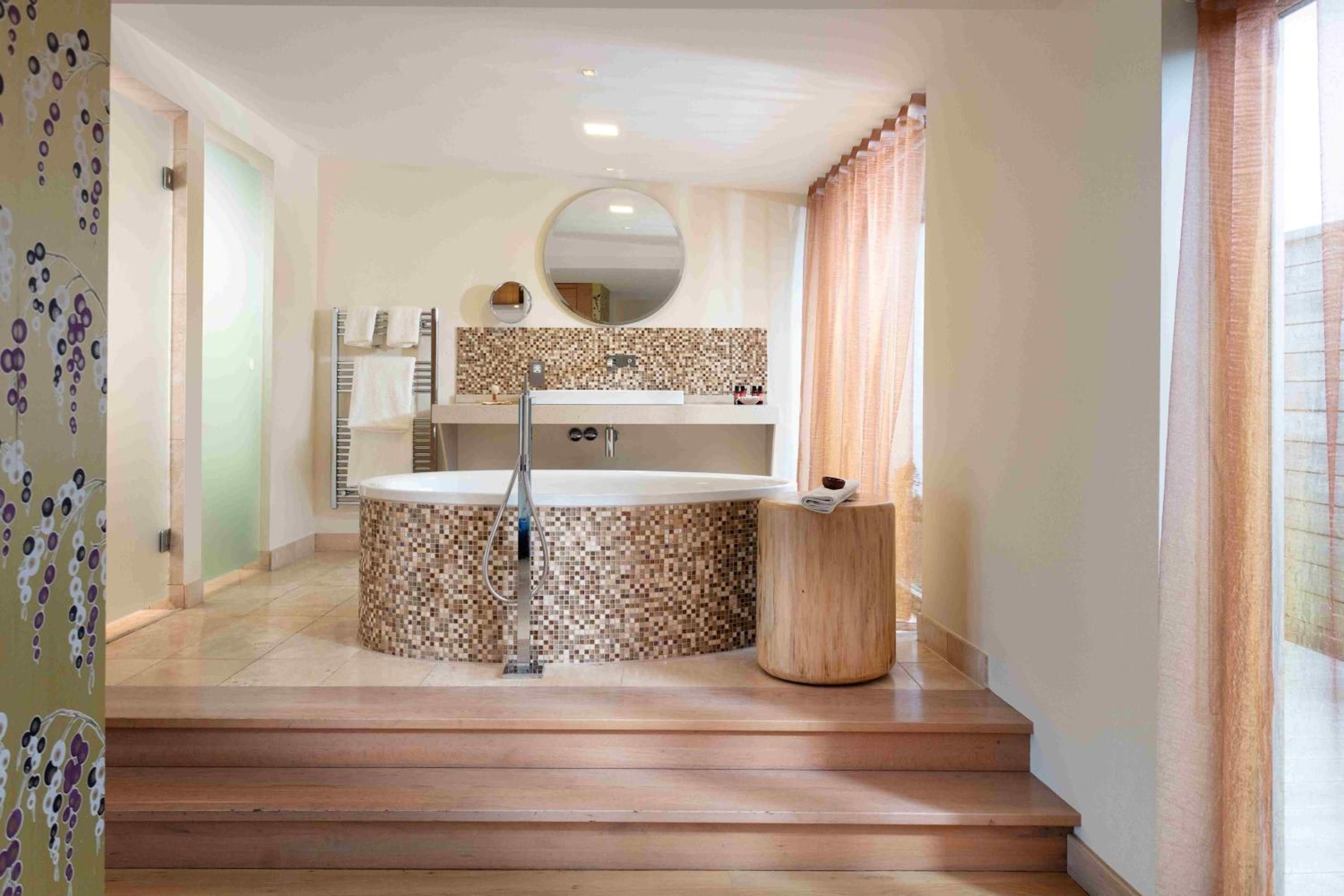 A bathroom with a freestanding bathtub, a round mirror, and a tiled backsplash.