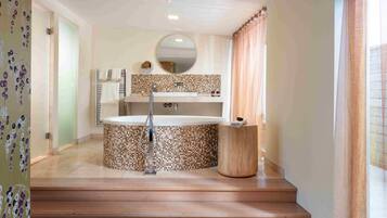 A bathroom with a freestanding bathtub, a round mirror, and a tiled backsplash.