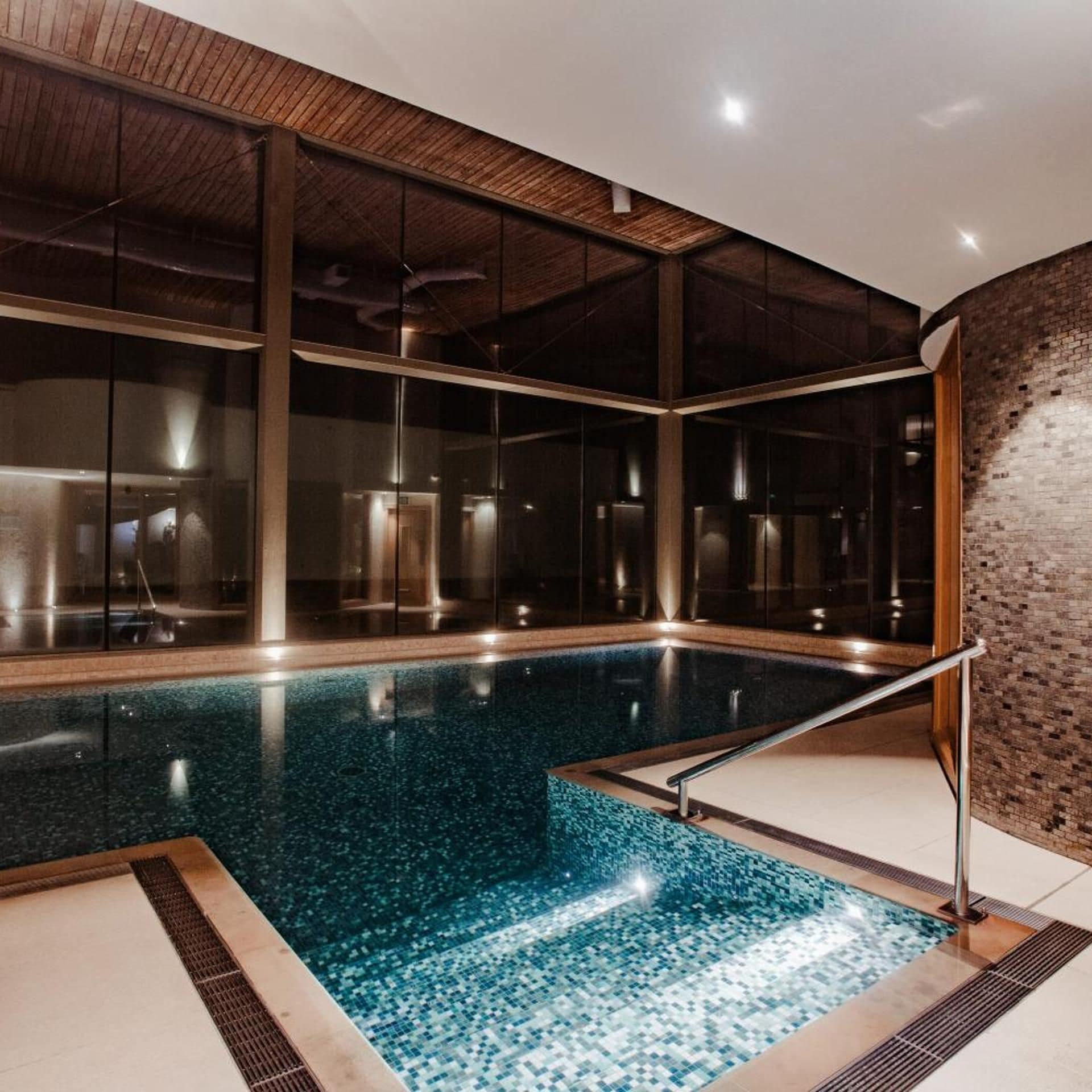 An indoor swimming pool with clear glass walls, a tiled floor, and a wooden ceiling.