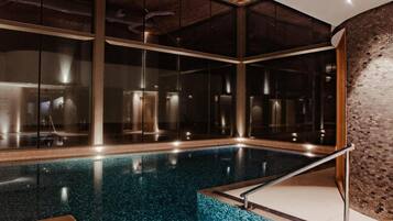 An indoor swimming pool with clear glass walls, a tiled floor, and a wooden ceiling.