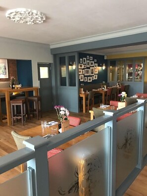 A restaurant with wooden tables and chairs, a bar area, and a wall decorated with framed pictures. - Strawberry Bank Hotel, NEC (Solihull)