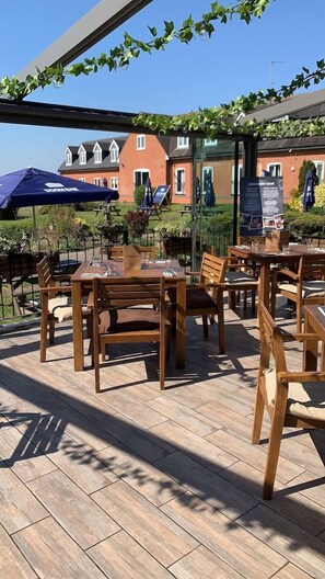 An outdoor patio with wooden tables and chairs, a covered seating area, and a view of a residential building in the background. - Strawberry Bank Hotel, NEC (Solihull)