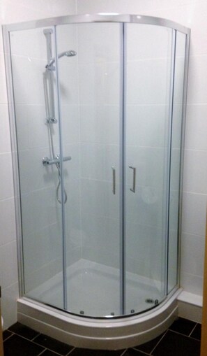 A glass-enclosed shower stall with a curved design, a handheld showerhead, and a single door. - Strawberry Bank Hotel, NEC (Solihull)