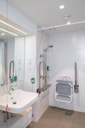 Un baño moderno con un lavamanos blanco, un cabezal de ducha manual y un asidero.