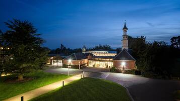 A church with a tall steeple, a brick building with a glass entrance, and a well-lit driveway.