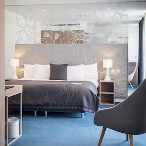 Una habitación de hotel moderna con una cama grande, dos mesitas de noche, una silla y un panel decorativo en la pared.