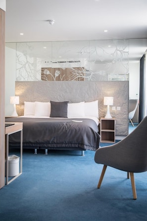 Ein modernes Schlafzimmer mit einem großen Bett, Nachttischlampen, einem Sessel und einer dekorativen Wandverkleidung.