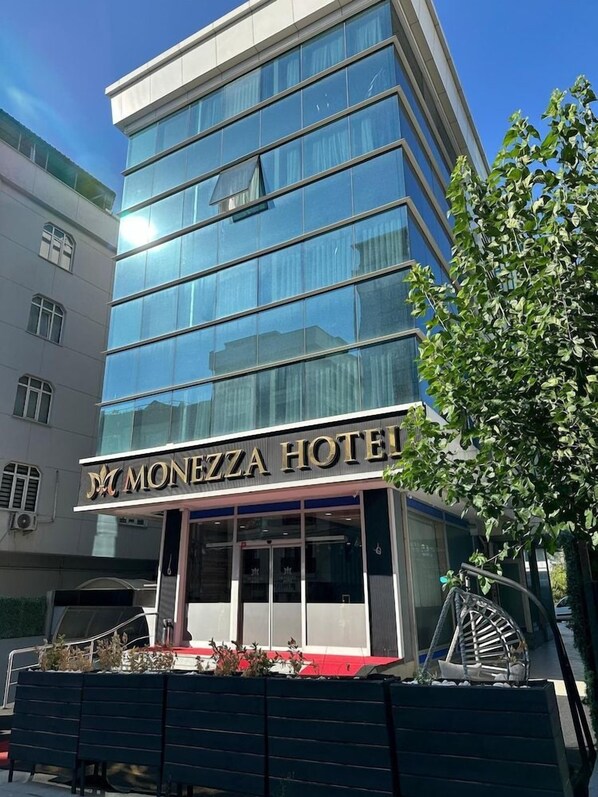 Un edifici d'hotel modern amb façana de vidre i un rètol que diu 'MONEZZA HOTEL'.