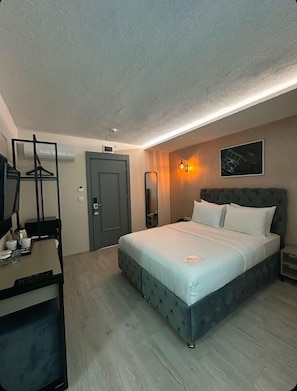 Hotellihuone, jossa on sänky, yöpöytä ja työpöytä tuolilla.