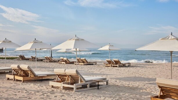 A beach with rows of sun loungers and umbrellas, a clear sky, and the ocean in the background. - Susurros del Corazon, Auberge Resorts Collection (Punta de Mita)