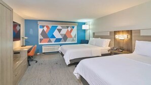 Habitació d'hotel amb dos llits, un escriptori, una cadira, un quadre abstracte gran i una tauleta de nit amb una làmpada.