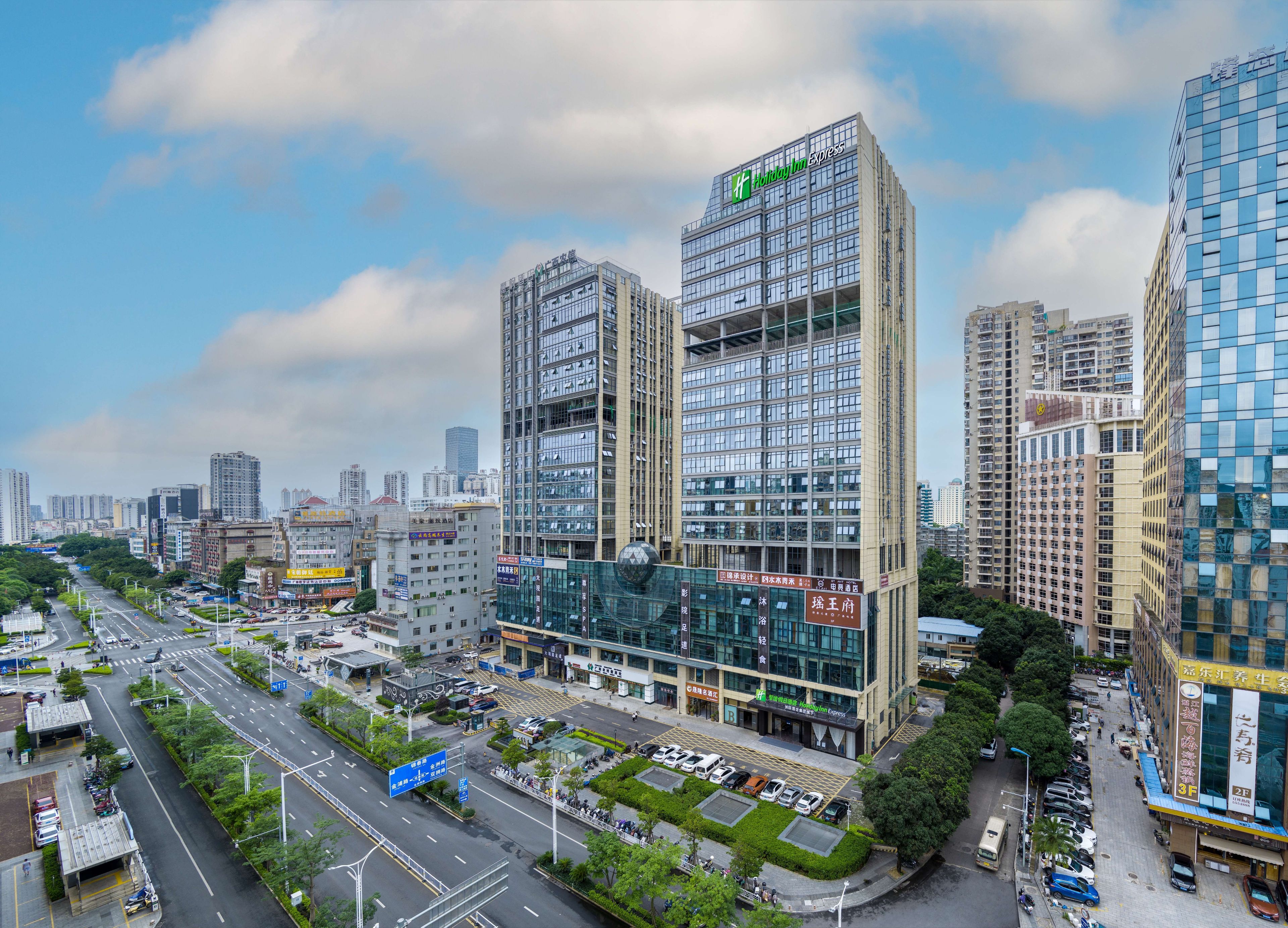 A modern hotel with a prominent sign, surrounded by high-rise buildings and a busy urban street.