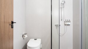 Une salle de bain moderne équipée de toilettes, d’une douche avec un pommeau de douche amovible et d’un panneau de commande fixé au mur.