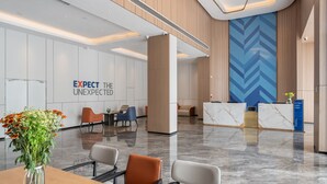 Un moderno vestíbulo de hotel con un mostrador de recepción, zona de estar y una pared con el texto 'EXPECT THE UNEXPECTED'.