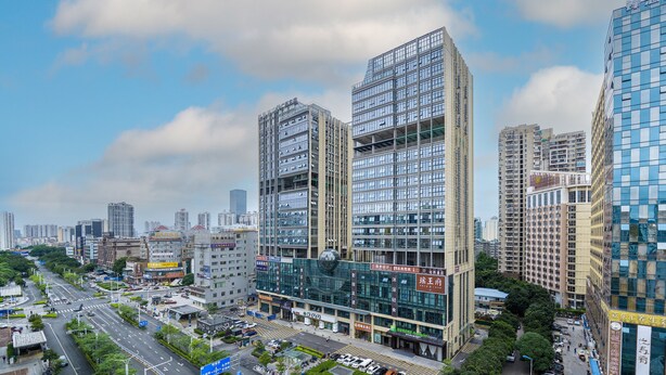 Un hotel de varios pisos con fachada de vidrio moderna, ubicado en una zona urbana concurrida y edificios altos circundantes.