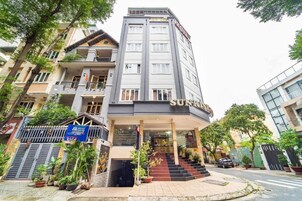 Um hotel com vários andares, uma entrada imponente, uma escadaria que leva à entrada e uma entrada com portão.