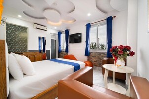 Quarto de hotel com cama, área de estar, televisão e janela com cortinas.