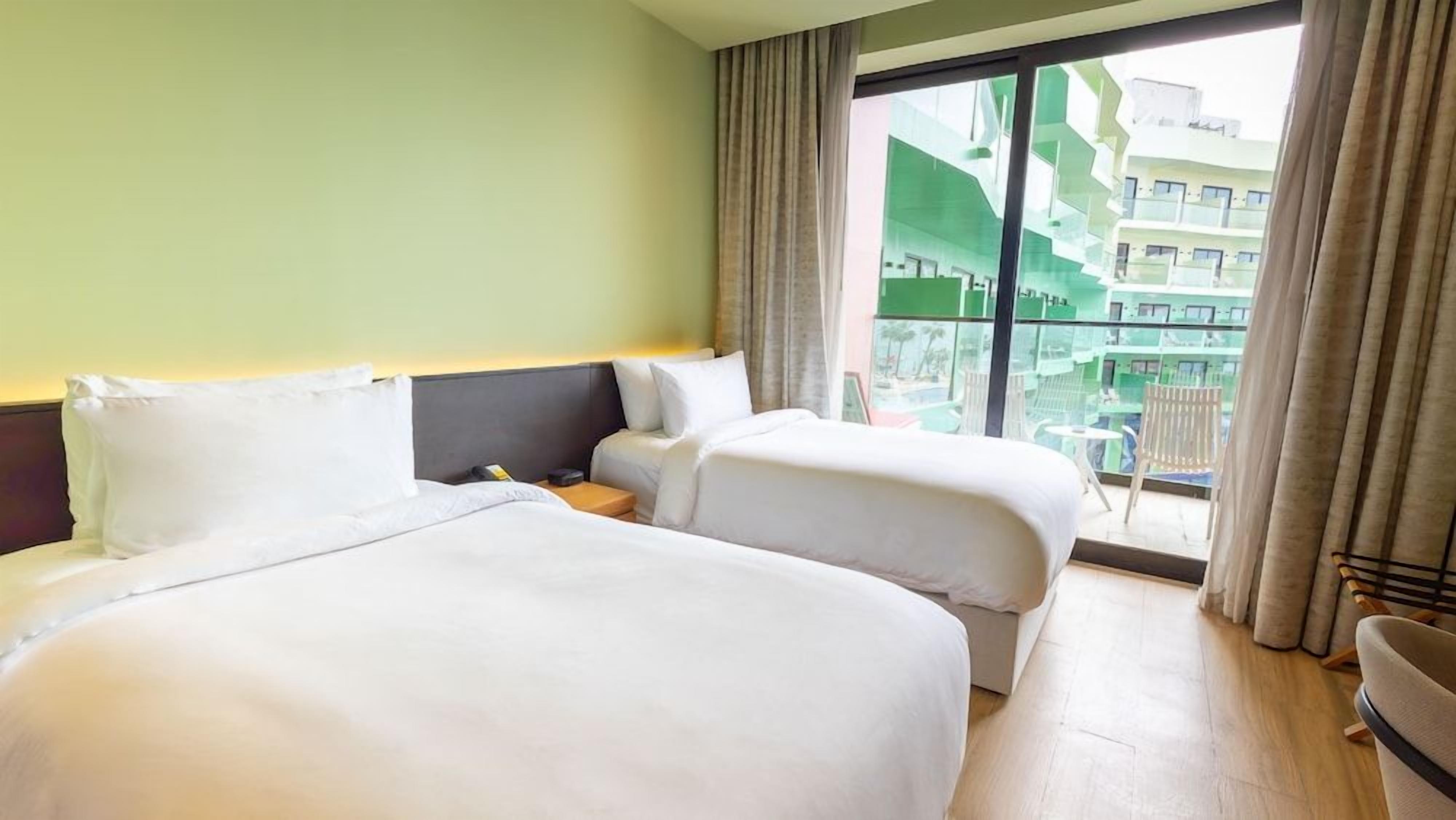 A hotel room with two beds, a nightstand, and a view of a building through a large window.