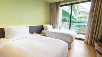 A hotel room with two beds, a nightstand, and a view of a building through a large window.