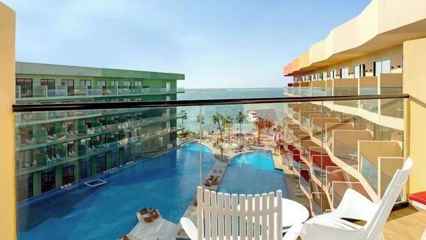 Een hotelbalkon met zwembad, met uitzicht op een resort en de zee.