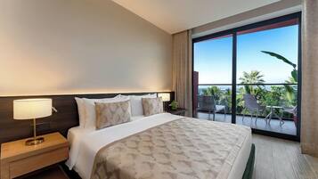 A hotel room with a large bed, a nightstand, a lamp, and a view of the outdoors through a balcony.
