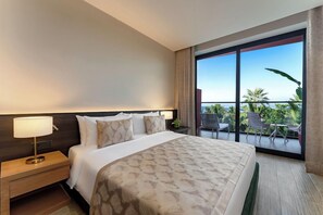 Habitación de hotel con una cama grande, una mesita de noche, una lámpara y vistas al exterior desde un balcón.