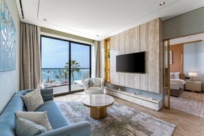 A modern hotel room with a large balcony, a flat-screen TV, a sofa, and a coffee table.