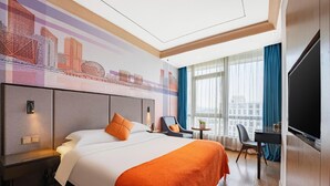 Ein Hotelzimmer mit einem großen Bett, einem Schreibtisch, einem Stuhl, einem Fernseher und einem Wandbild mit Stadtansicht.