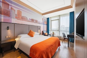Habitación de hotel con una cama grande, un escritorio, una silla, un televisor y un mural con vista a la ciudad en la pared.