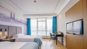 Ein Hotelzimmer mit zwei Betten, einem Schreibtisch, einem Fernseher und einem Wandgemälde mit Stadtansicht.