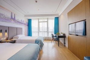 Habitación de hotel con dos camas, un escritorio, un televisor y un mural con vista a la ciudad.